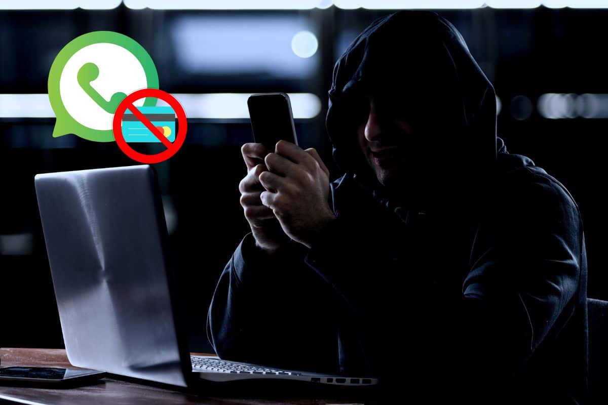 Hombre encapuchado sostiene su movil frente a un ordenador hackear WhatsApp online gratis sin tarjeta de crédito